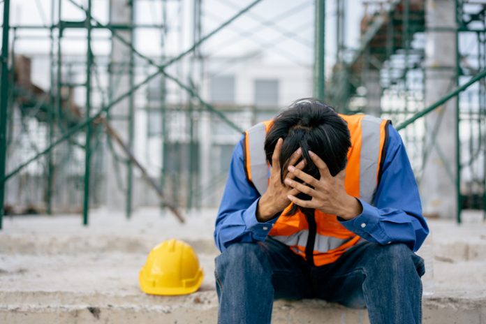 Foreman sitting hold the head with hands in factory construction site, tired fatigue exhaustion worker hard, suffering stress, upset, having problems as work, depression, have a headache, heat stroke